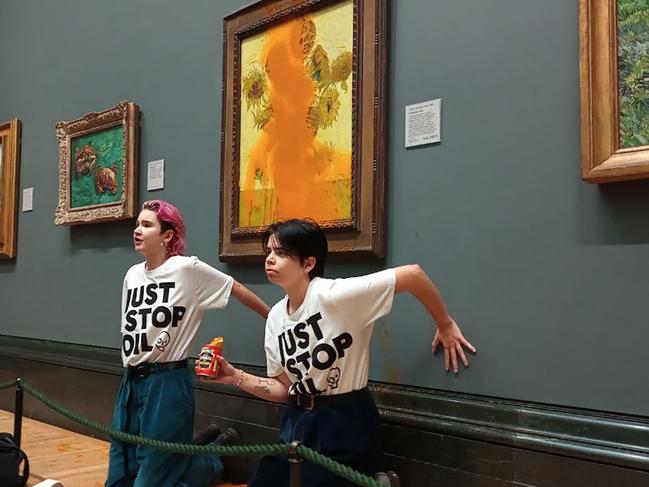 A handout picture from the Just Stop Oil climate campaign group shows activists with their hands glued to the wall under Vincent van Gogh's "Sunflowers" after throwing tomato soup on the painting at the National Gallery in central London on October 14, 2022. - London's Metropolitan Police said its officers arrested two protesters from the Just Stop Oil group for criminal damage and aggravated trespass after they "threw a substance over a painting" at the gallery on Trafalgar Square. (Photo by Handout / Just Stop Oil / AFP) / RESTRICTED TO EDITORIAL USE - MANDATORY CREDIT "AFP PHOTO /  JUST STOP OIL " - NO MARKETING - NO ADVERTISING CAMPAIGNS - DISTRIBUTED AS A SERVICE TO CLIENTS