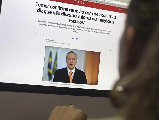 A woman watches a pronouncement by Brazil's President Michel Temer on a computer screen, about his possible involvement with the Brazilian construction giant Odebrecht, in Brasilia, Brazil, Thursday, April 13, 2017. Brazilian construction giant Odebrecht paid millions in bribes to President Michel Temer's party and another party, to ensure a contract with the state oil company, according to plea bargain testimony from a former executive at the company, released Wednesday, as part of the biggest corruption probe in Brazil's history. (AP Photo/Eraldo Peres)