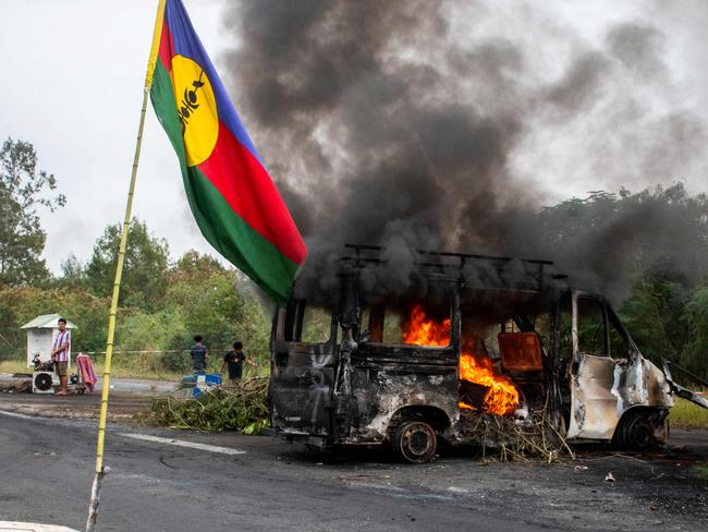 This photograph shows a Kanak flag waving next to a burning vehicle at an independantist roadblock at La Tamoa, in the commune of Paita, France's Pacific territory of New Caledonia on May 19, 2024. French forces smashed through about 60 road blocks to clear the way from conflict-stricken New Caledonia's capital to the airport but have still not reopened the route, a top government official said on May 19, 2024. (Photo by Delphine Mayeur / AFP)