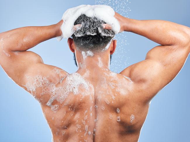 Shower, washing hair and back of man in studio for cleaning, hygiene and skincare on blue background. Dermatology, bathroom and person with shampoo, soap and foam for wellness, health or self care