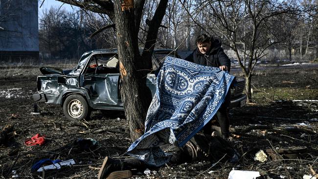 A man uses a carpet to cover a body stretched out on the ground after bombings on the eastern Ukraine town of Chuguiv.