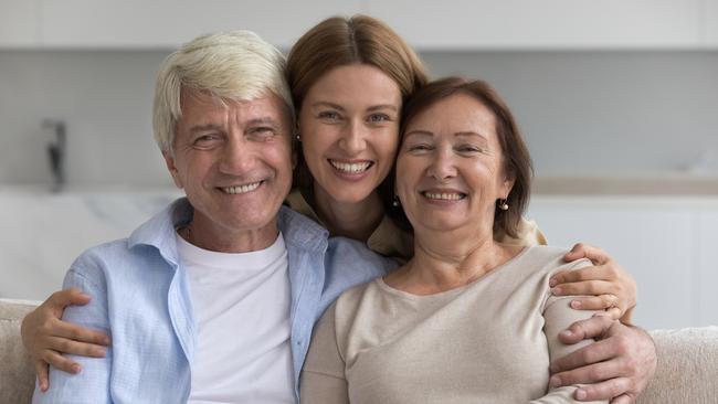 Happy pretty adult woman hugging positive older parents with love, care, support, affection, looking at camera, smiling, enjoying meeting at home, good relationship, bonding. Family portrait; senior couple early inheritance generic