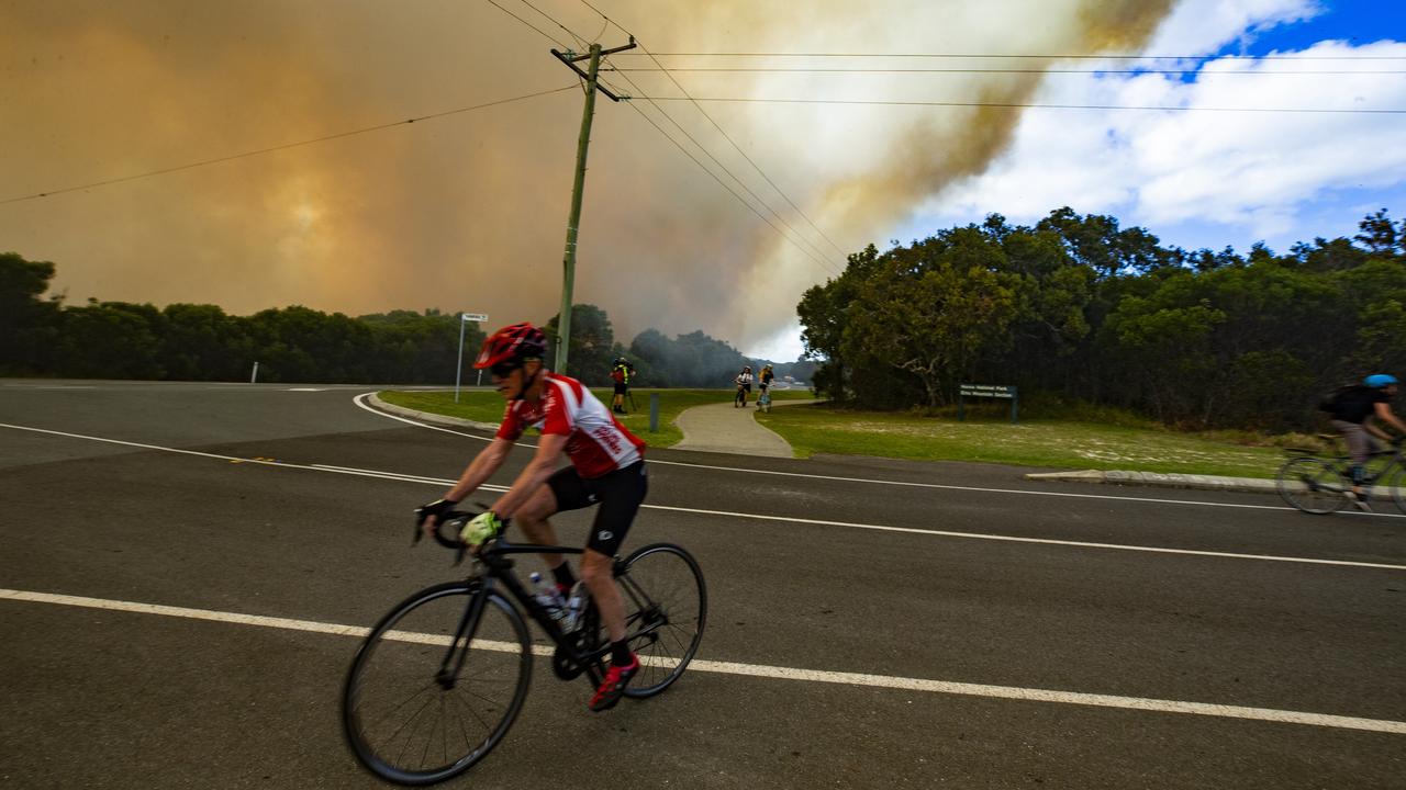 Smoke from a bushfire between Coolum and Peregian Beach dwarfs a cyclist on his morning journey . Picture: Lachie Millard