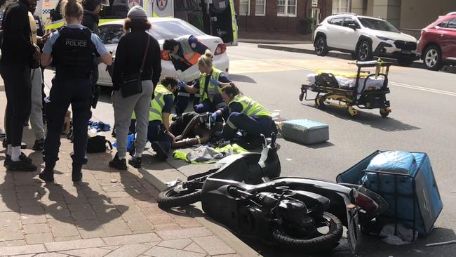 NSW Ambulance paramedics work to stabilise a scooter delivery rider who suffered a serious leg injury in a collision with a car driven by a rideshare driver on West Esplanade, Manly, on Wednesday afternoon. Picture: Jim O’Rourke