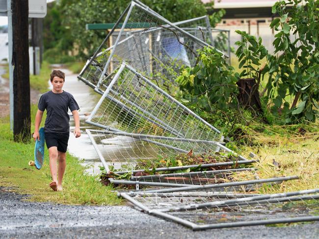 A boy walks past a fence brought down by Tropical Cyclone Marcia along a road in Yeppoon.