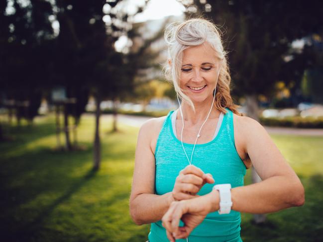Fit senior woman listening to music and checking her pulse and jogging time on smartwatch