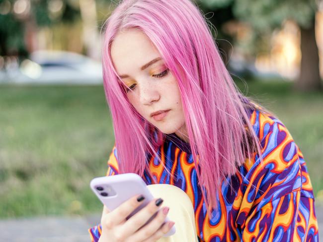 Pink-haired teenage hipster girl in a colorful bright T-shirt is using a smartphone on a summer day.Summer concept.Generation Z style.Social media concept.