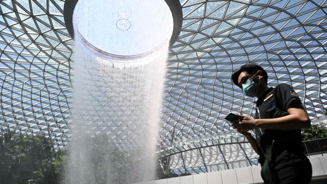 A man wearing a protective face mask walks past the Rain Vortex display at Jewel Changi Airport in Singapore. Picture: Roslan Rahman/AFP