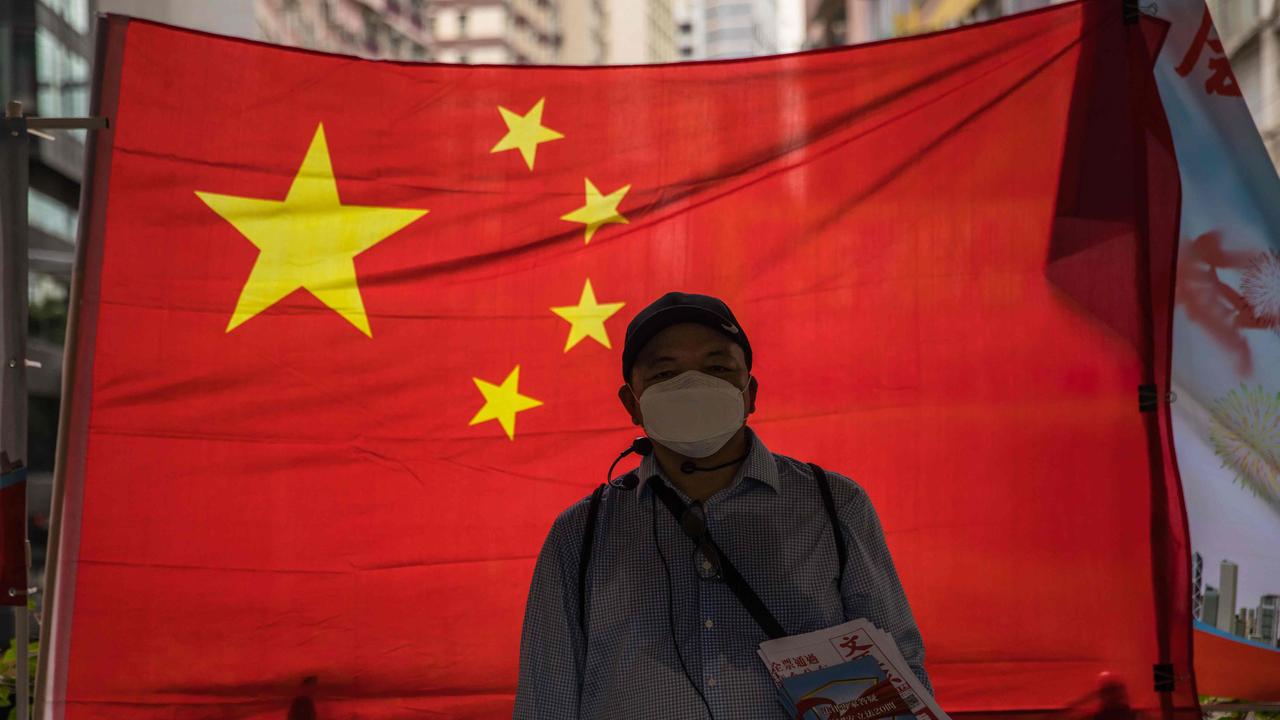 A pro- Beijing government supporter hands out newspapers in front of a Chinese flag in Hong Kong last week. Picture: DALE DE LA REY / AFP.