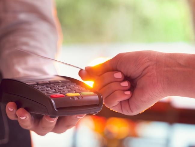 Woman paying with a credit card. She is using a contactless tapping eftpos system. Image is backlit with lens flare. Close up . Picture: iStock