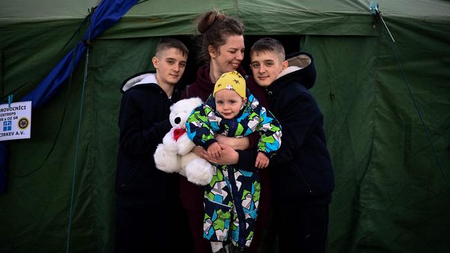 TOPSHOT - Ukrainian refugee Tetyana Dzymik (C), a 38-year-old drawing teacher from a village near Bucha, poses for a picture along with her children, twins Ivan and Danylo, and baby Oleksiy, as they stand at the entrance to an NGO tent after crossing the Ukrainian-Slovakian border into Slovakia at the Vysne Nemecke border crossing, eastern Slovakia on April 8, 2022. - A heartbreaking human drama is playing out along Ukraine's borders -- fleeing refugees pass the homesick going back, while others who left and then returned flee for their lives for a second time. (Photo by Christophe ARCHAMBAULT / AFP)