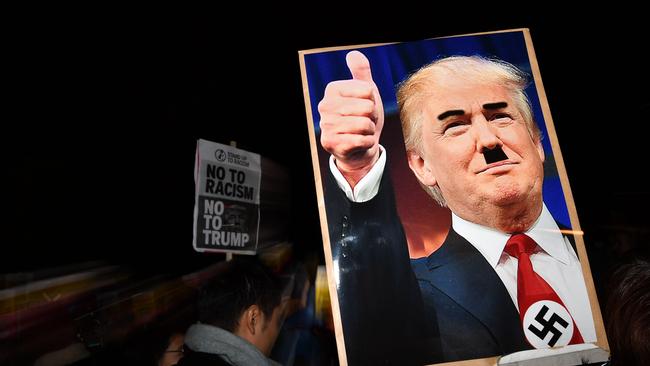 TOPSHOT - A demonstrator holds a placard showing a picture of US President-elect Donald Trump modified to add a swastika and an Adolf Hitler-style moustache during a protest outside the US Embassy in London November 9, 2016 against Trump after he was declared the winner of the US presidential election.  Political novice and former reality TV star Donald Trump has defeated Hillary Clinton to take the US presidency, stunning America and the world in an explosive upset fueled by a wave of grassroots anger. / AFP PHOTO / BEN STANSALL