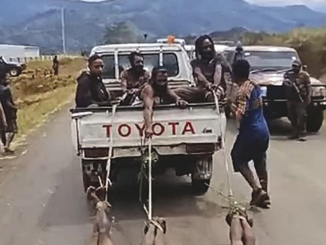 A warring tribe drags the bodies of three opponents behind a ute.