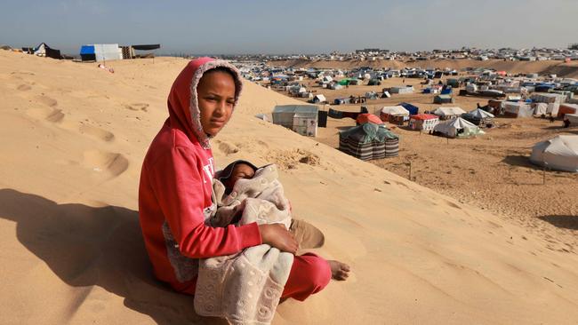 A Palestinian girl sits holding a toddler on a sand dune overlooking a camp for displaced people in Rafah in the southern Gaza Strip on Sunday. Picture: AFP