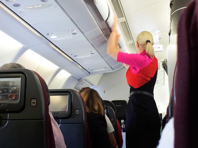 Brisbane - Oct 31 2022: Qantas airways female flight attendant closing the overhead luggage compartment lid for carry on baggage before take off.In Australia 1 flight attendant for every 36 passengers