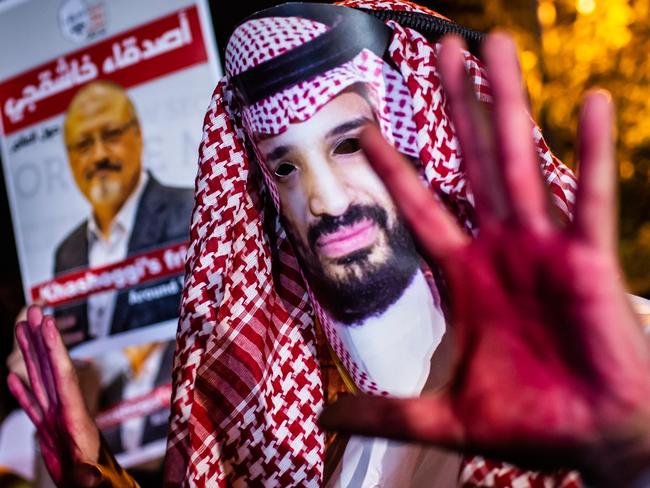 A protestor wears a mask of depicting Saudi Crown Prince Mohammad Bin Salman with red painted hands next to people holding posters of Saudi journalist Jamal Khashoggi  during the demonstration outside the Saudi Arabia consulate in Istanbul, on October 25, 2018. - Jamal Khashoggi, a Washington Post contributor, was killed on October 2, 2018 after a visit to the Saudi consulate in Istanbul to obtain paperwork before marrying his Turkish fiancee. (Photo by Yasin AKGUL / AFP)