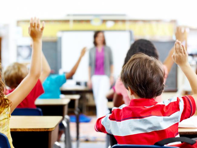 Rear-view of students raising their hands to answer the teacher's question