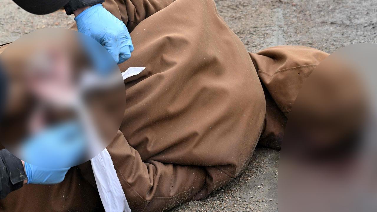 A communal worker releases the wrists of a dead man with his hands tied behind his back in the town of Bucha, not far from the Ukrainian capital Kyiv. Picture: Sergei Supinsky/AFP