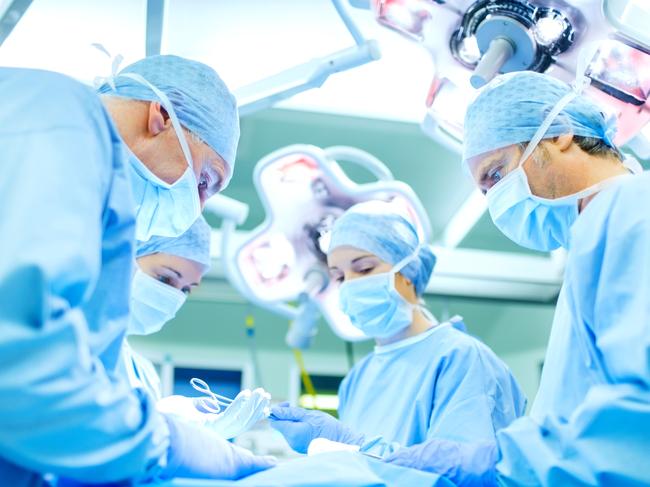 Team of surgeons performing surgery on patient in operating room at hospital. Horizontal shot.