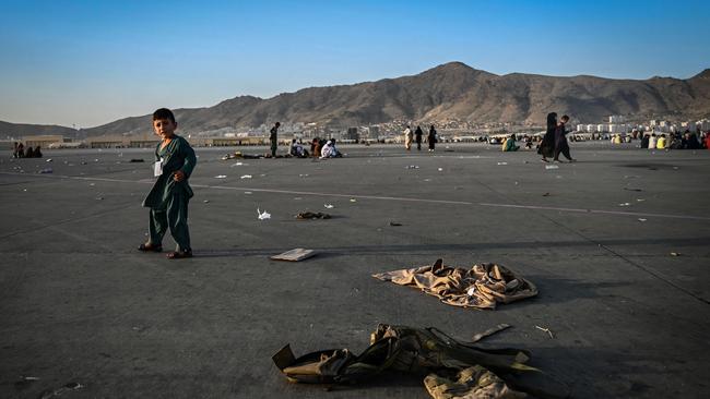 An Afghan child walks near military uniforms as he with elders wait to leave the Kabul airport. Picture: AFP