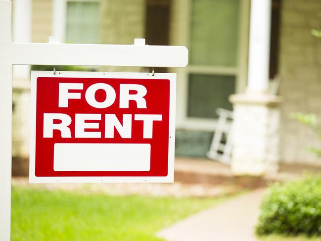 Red and white "House for Rent" sign in front of a stone, wood house that is a rental property. Green grass and bushes indicate the spring or summer season. Front porch and windows in background. Real estate sign in residential neighborhood.  Moving house, relocation concepts.