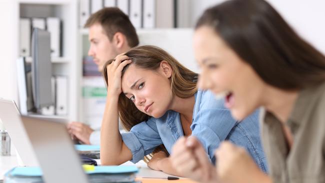 Worried worker beside a successful one who is excited reading good news on line at office. Picture: iStock