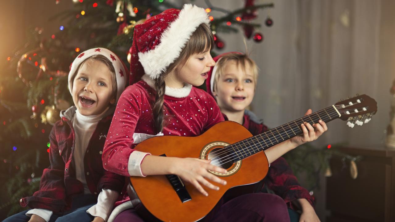Young children sings carols in front of their Christmas tree.