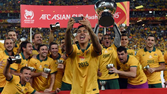 Australia's Massimo Luongo (C) takes a selfie as the team celebrates with the AFC Asian Cup football trophy after beating South Korea at Stadium Australia in Sydney on January 31, 2015. AFP PHOTO / Saeed KHAN -- IMAGE RESTRICTED TO EDITORIAL USE - STRICTLY NO COMMERCIAL USE