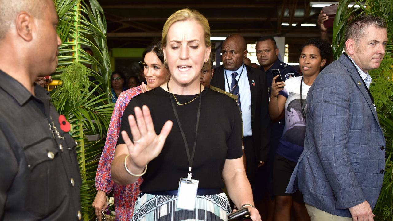 Security personnel guide Meghan through the crowded market. Picture: Ian Vogler
