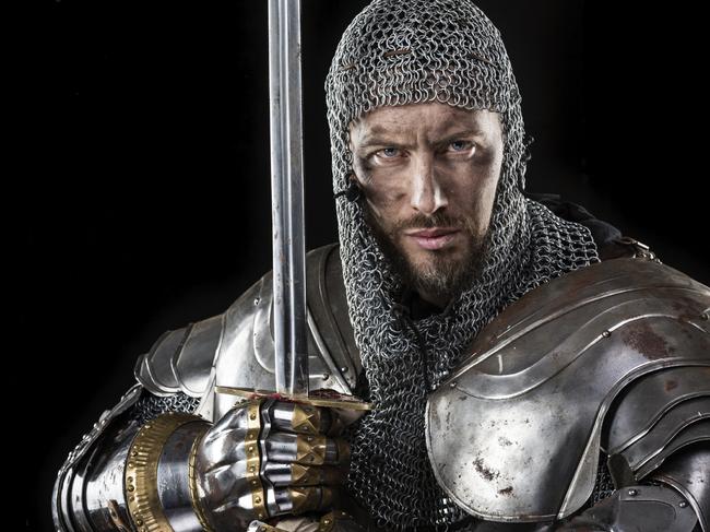 Portrait of Medieval Dirty Face Warrior with chain mail armour and red cross on sword. Black Background