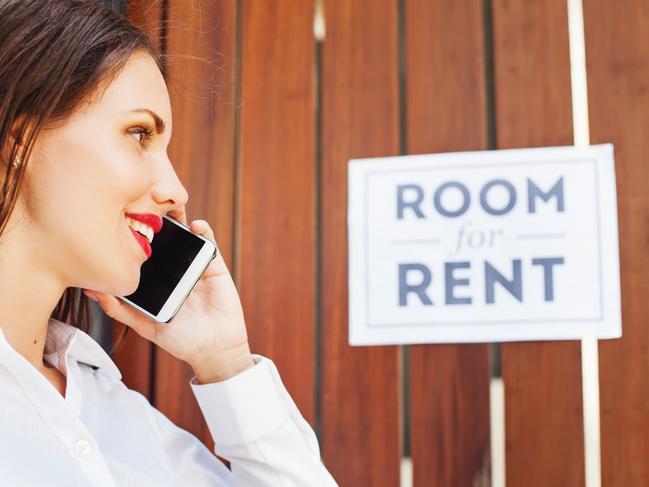 caucasian woman in white shirt standing in front of wooden fencing with "room for rent" ads and calling to house owner