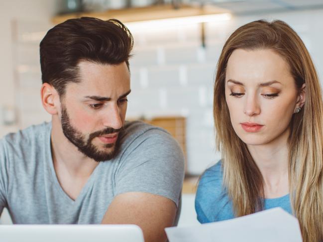 Young couple worried about their finances at home. They are wearing pajamas and drinking first coffee of the day at the kitchen.