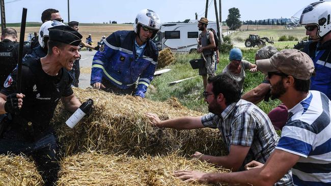 A French policeman holding a baton and tear gas spray yells at protesting farmers.