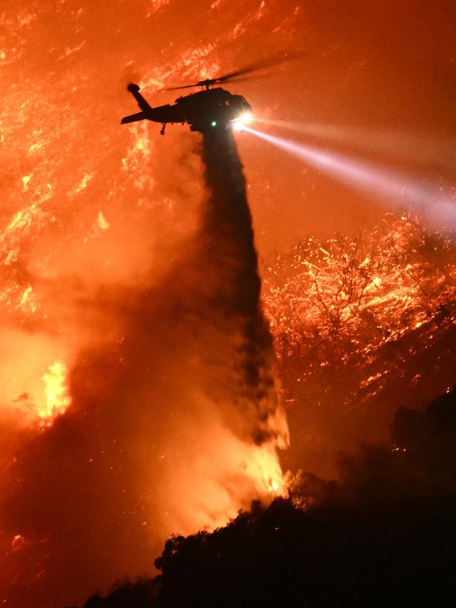 A fire fighting helicopter drops water as the Palisades fire grows near the Mandeville Canyon neighbourhood and Encino, California. Picture: Patrick T. Fallon / AFP