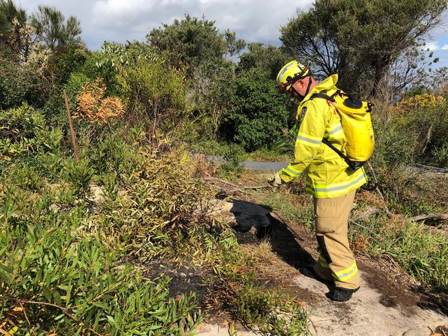 A NSW Fire & Rescue firefighter douses smoldering embers with a water sprayer the day after the hazard reduction burn-off.