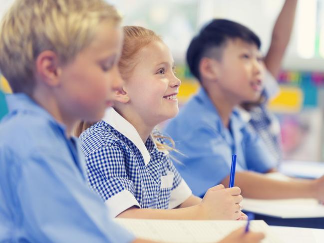 Group of children listening to the teacher. They are in a classroom. Multiethnic group with Caucasian and Asian kids. School girl is smiling and happy