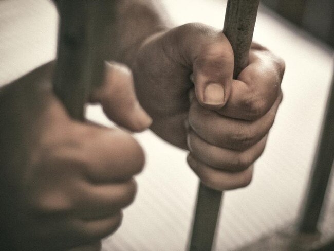 Man's hands tightly holding the bars of his jail cell.