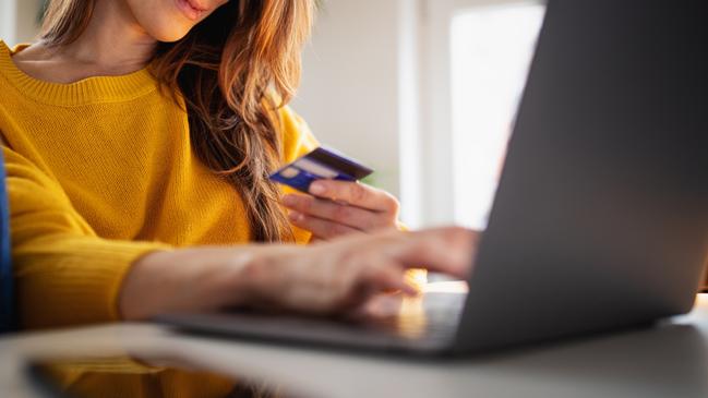 A beautiful young woman enjoying working at home on her laptop in cozy and bright apartment wearing yellow sweater and shopping online paying with credit card