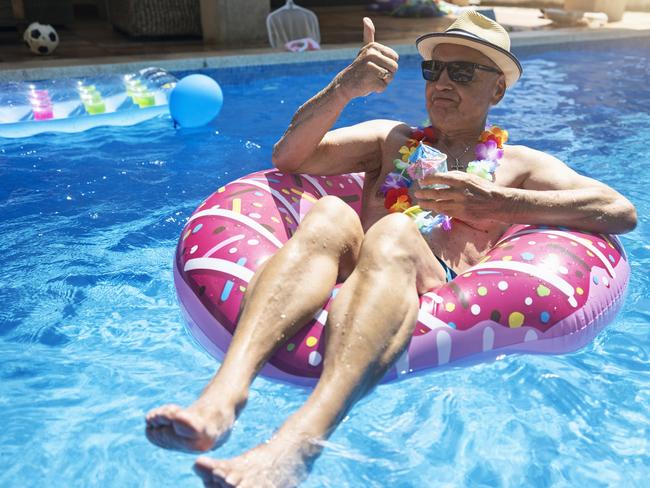 Senior man relaxing in floating ring in the swimming pool. He is drinking juice cocktails; Generic wealthy retiree money