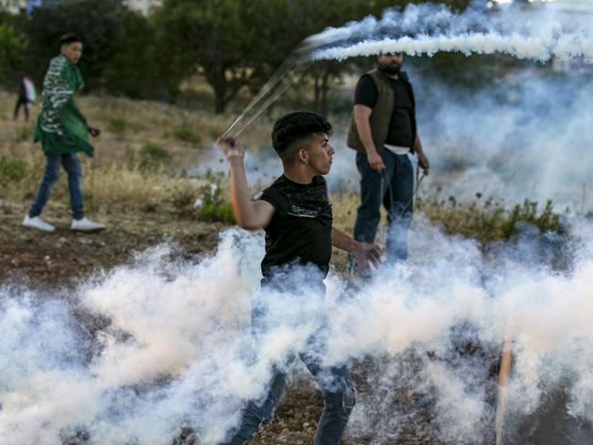 Masked Palestinian protesters use slingshots to throw back tear gas canisters at Israeli security forces during clashes following a demonstration against Israel's plan to annex parts of the occupied West Bank, at the northern entrance of the West Bank city of Ramallah near the Jewish settlement of Beit El, on July 1, 2020. - Thousands of Palestinians protested across the Palestinian territories against Israel's West Bank annexation plans, as Prime Minister Benjamin Netanyahu said talks were ongoing on the controversial project facing intensifying international opposition. Demonstrations were held in the West Bank cities of Ramallah and Jericho, attended by a handful of left-wing Israeli politicians opposed to annexation. (Photo by ABBAS MOMANI / AFP)