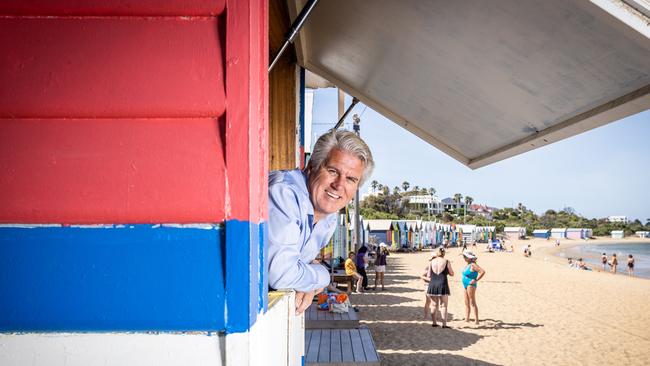 Real estate agency director Nick Johnstone a bathing box on the Brighton foreshore, painted in his football team’s signature colours. Picture: Jake Nowakowski