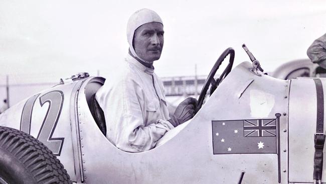 Freddie McEvoy in his Maserati at New York's 1936 Vanderbilt Cup, proudly displaying the Australian flag. It was his need for speed that earnt him the nickname “Suicide Freddie”, and a place leading the British Olympic bobsleigh team into Nazi Germany’s Winter Olympic Games. Picture: Reproduced with permission from The Scandalous Freddie McEvoy, by Frank Walker (Hachette)