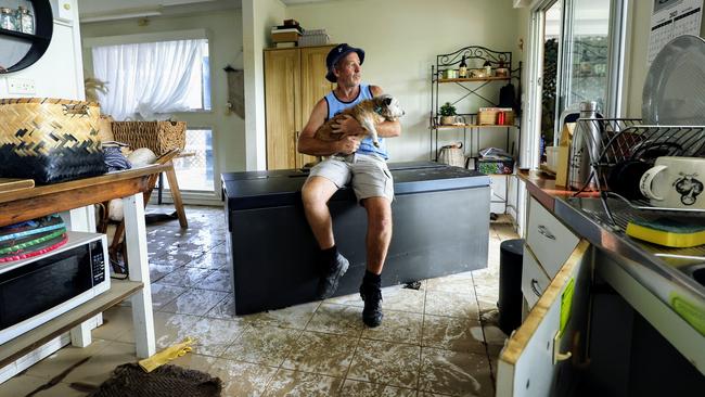 Chris Tress sits on his upturned refrigerator with his dog Peg in his kitchen that was flooded in Mimosa Street, Holloways Beach. The beachside suburb suffered widespread flooding this week when heavy rain from ex Tropical Cyclone Jasper caused the Barron River to breach its banks. Picture: Brendan Radke