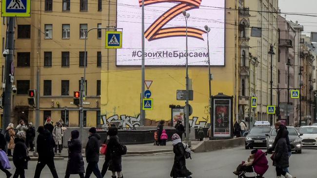 Pedestrians cross a street in front of a billboard displaying the symbol "Z" in the colours of the ribbon of Saint George and a slogan reading: "We don't give up on our people", in support of the Russian armed forces, in Saint Petersburg, on March 7. Picture: AFP