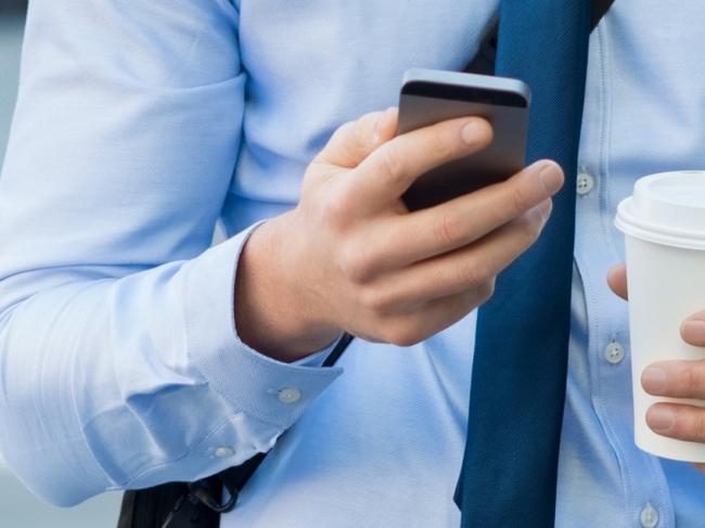 Businessman using smartphone and holding paper cup ina urban scene. Worried businessman in walking on the road and messaging with phone. Young man text messaging through cell phone while walking on the road in the city centre.