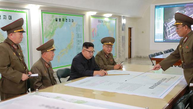 North Korean leader Kim Jong-un is pictured with plans to launch ballistic missiles towards the US territory of Guam. The map in front of him details the flight path of a missile from North Korea towards the strategically significant Pacific island. Picture: KCNA/AFP