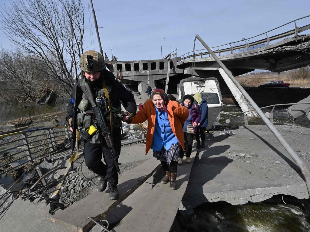 A Ukrainian police officer helps an elderly woman to cross a destroyed bridge as she evacuates Irpin, northwest of Kyiv. Picture: Sergei Supinsky / AFP