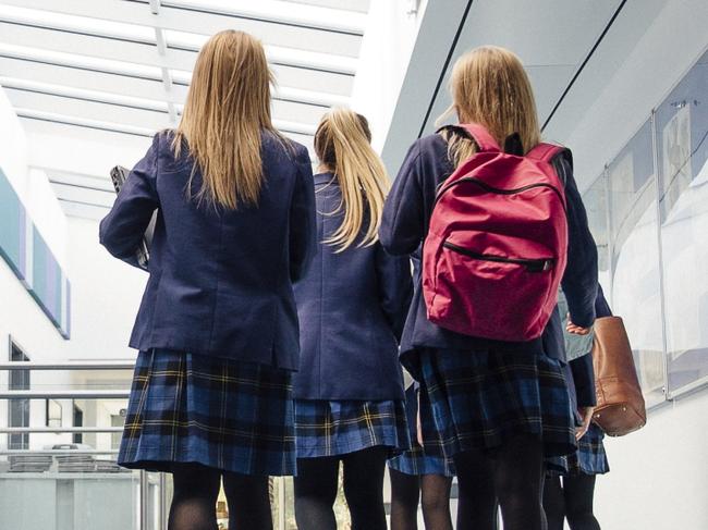 Group of students are walking down the corridor of their school. There is a female teacher using the printer.