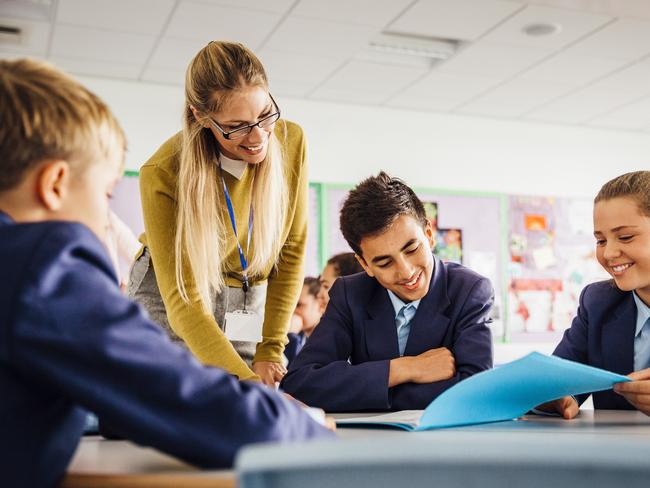 Female teacher with her students. Teenage students sitting around a table while their teacher stands over them smiling. Low angle view point