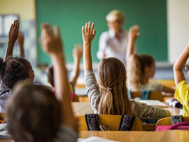 Rear view of large group of students raising their arms to answer the question on a class at elementary school.